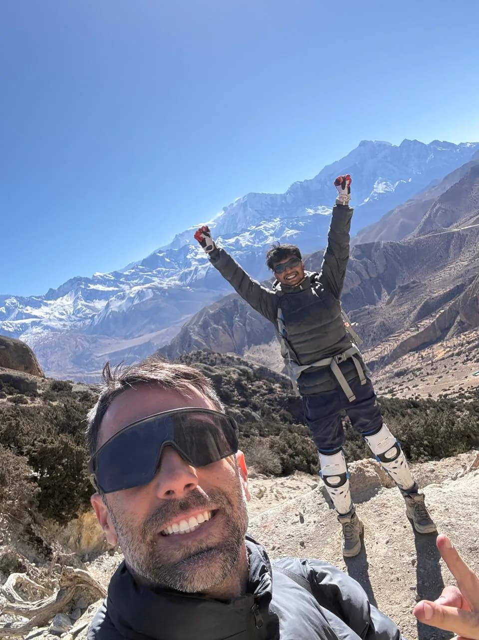 A guest photographs Rohit in full riding armour with his arms raised on the Mustang road, a glaciated peak behind him