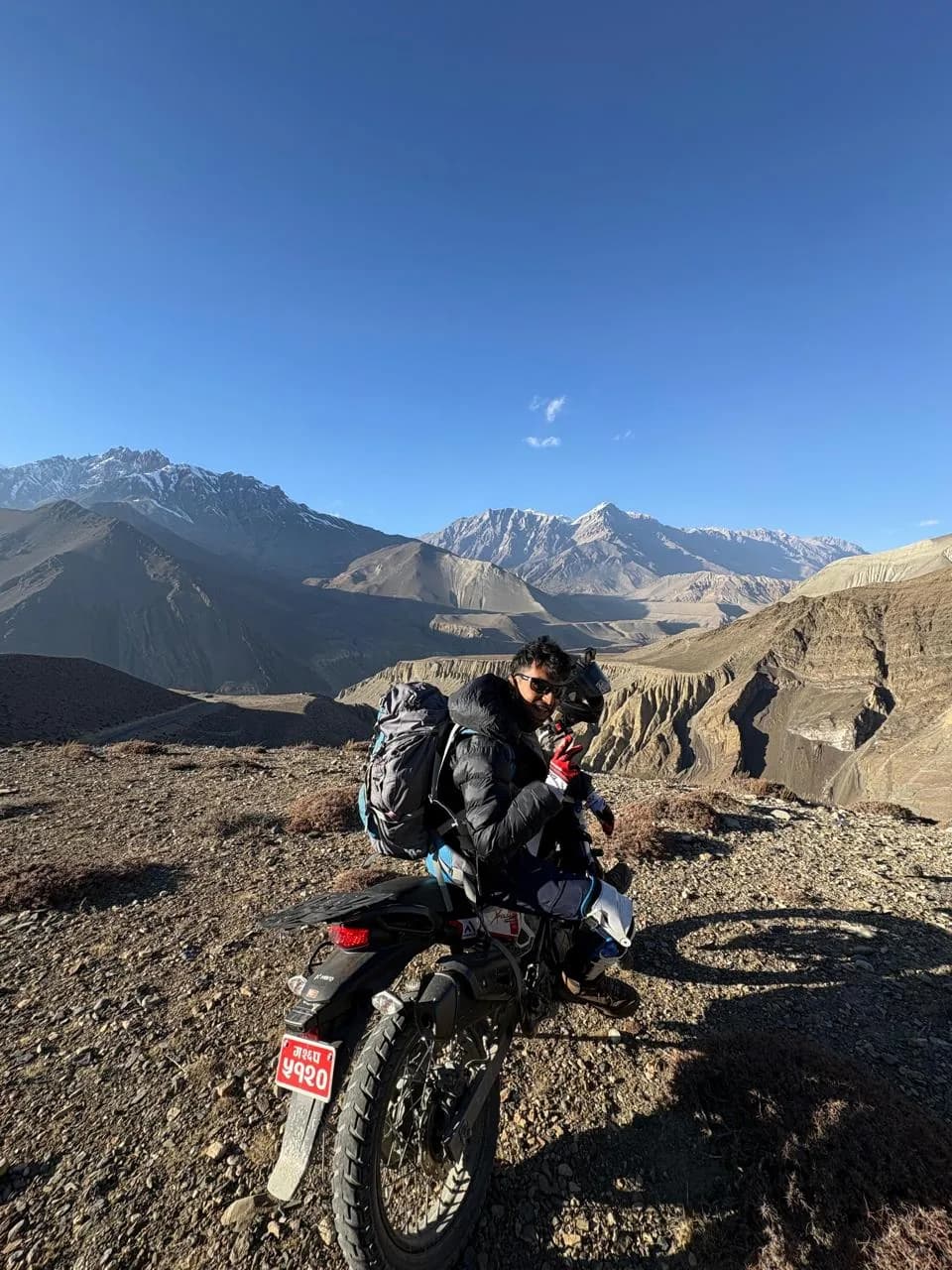 Rohit sitting on a loaded trail bike with a trekking pack strapped to the seat on the dirt road through Mustang