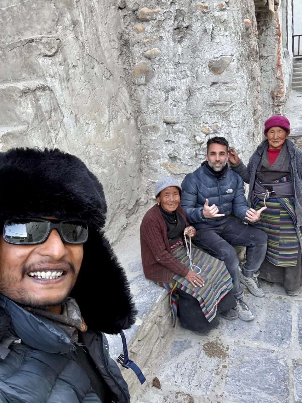 Rohit and a guest sitting with two Mustang village elders in traditional Tibetan dress against a whitewashed stone wall